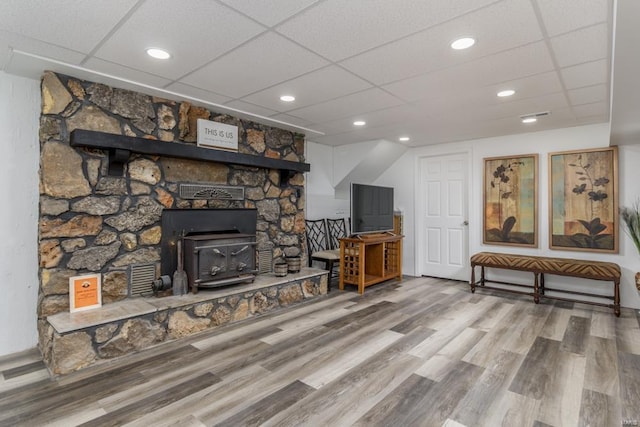 living room featuring hardwood / wood-style floors, a drop ceiling, and a wood stove