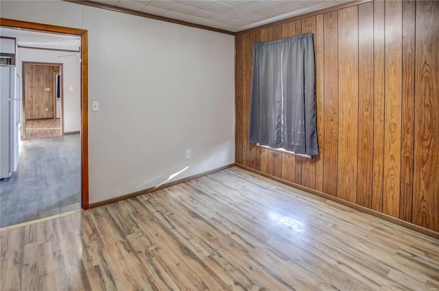 unfurnished room with ornamental molding, wooden walls, baseboards, and wood finished floors