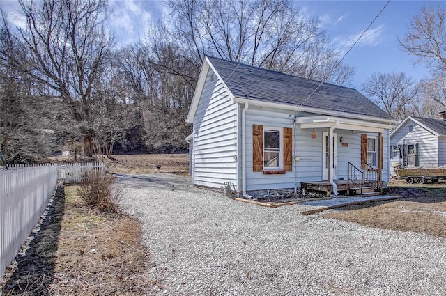 view of front of property with gravel driveway, a shingled roof, and fence