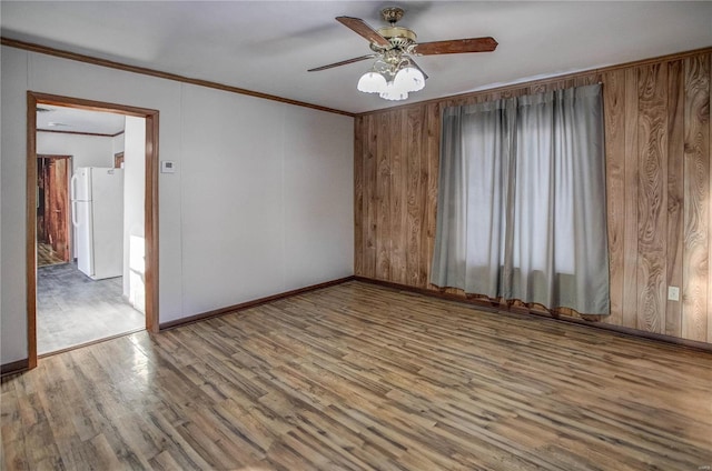 spare room with crown molding, ceiling fan, wooden walls, wood finished floors, and baseboards