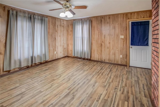 spare room featuring ceiling fan, wooden walls, wood finished floors, and baseboards