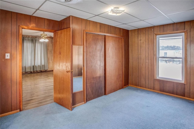 unfurnished bedroom featuring a closet, carpet flooring, a paneled ceiling, and wooden walls