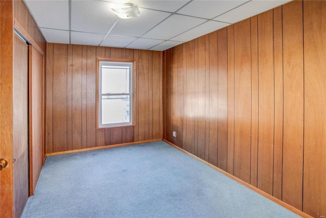 carpeted spare room with a paneled ceiling and wooden walls