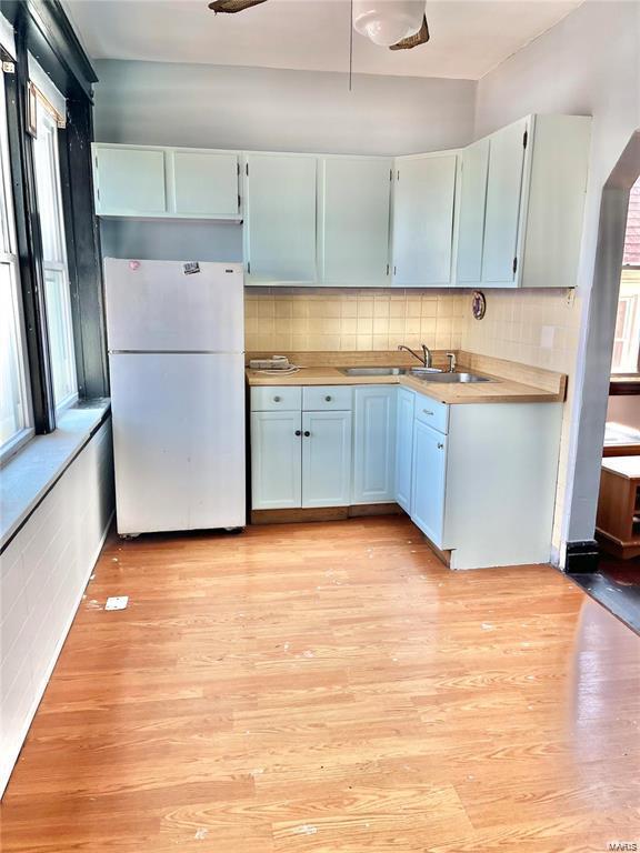 kitchen with light wood-type flooring, white refrigerator, tasteful backsplash, and sink