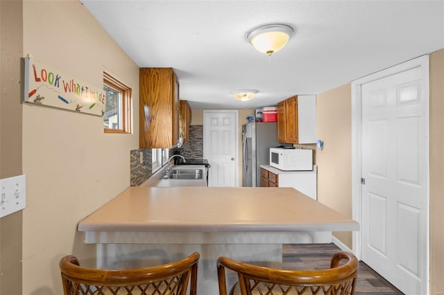 kitchen featuring kitchen peninsula, dark hardwood / wood-style floors, decorative backsplash, stainless steel refrigerator, and sink