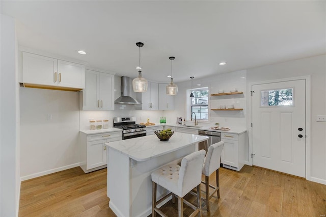 kitchen featuring wall chimney exhaust hood, white cabinetry, a center island, hanging light fixtures, and appliances with stainless steel finishes