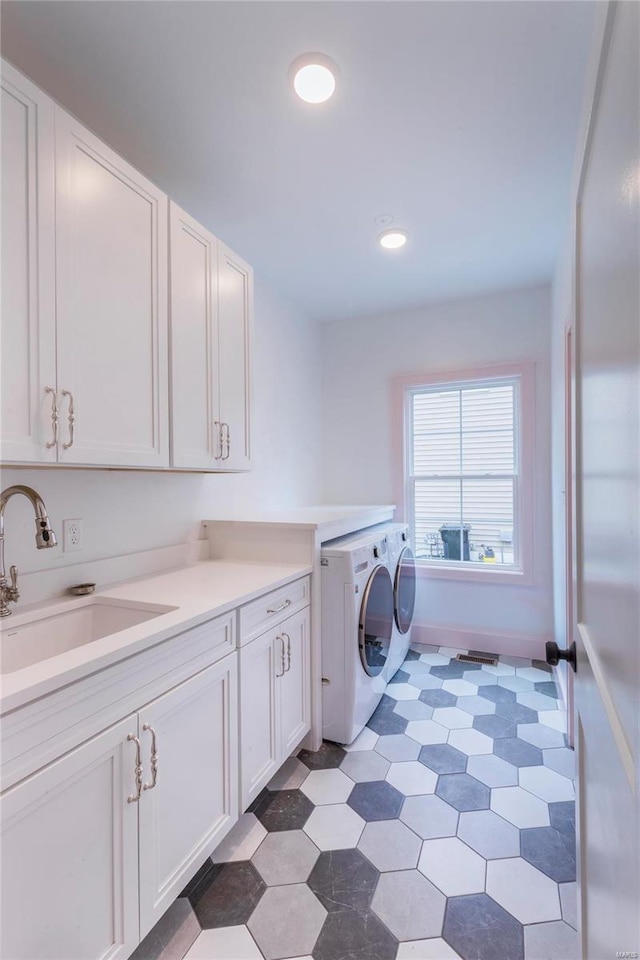 clothes washing area featuring sink, washing machine and dryer, and cabinets