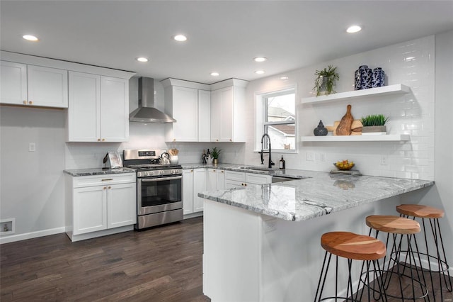 kitchen featuring sink, stainless steel gas range oven, white cabinetry, light stone counters, and wall chimney range hood