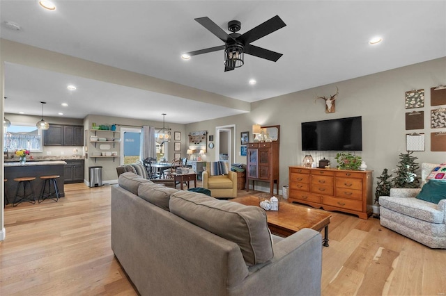 living room featuring ceiling fan with notable chandelier and light hardwood / wood-style flooring