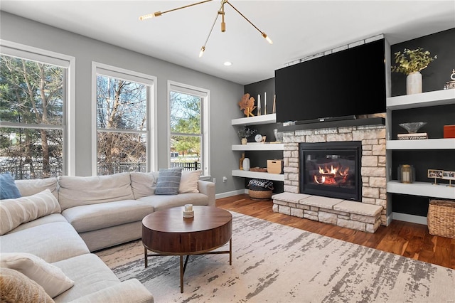 living room with built in features, a stone fireplace, wood-type flooring, and a chandelier