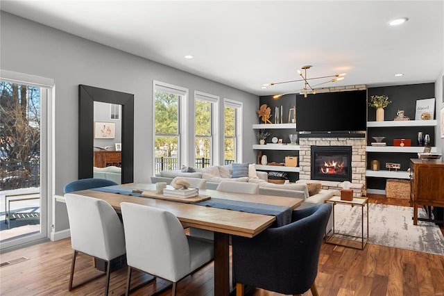 dining area with a stone fireplace, hardwood / wood-style floors, built in shelves, and a notable chandelier