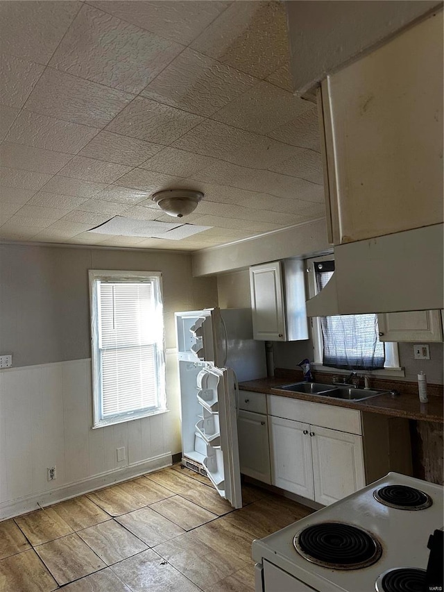 kitchen featuring sink, white cabinetry, white electric stove, and wood walls