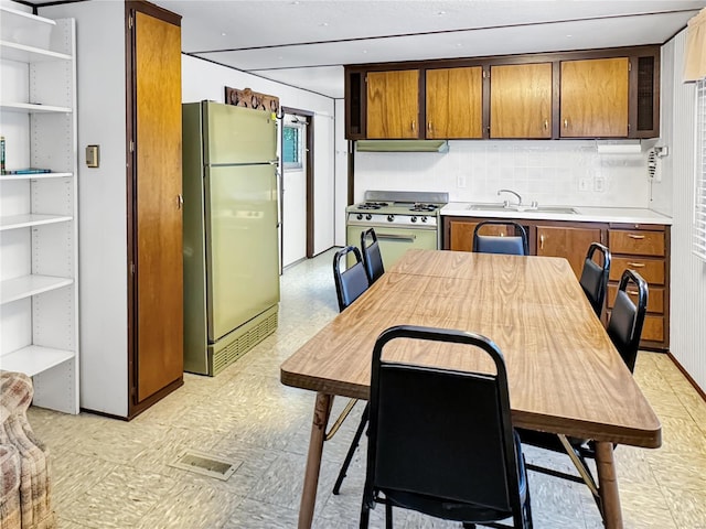 kitchen with refrigerator, range hood, sink, decorative backsplash, and gas range oven