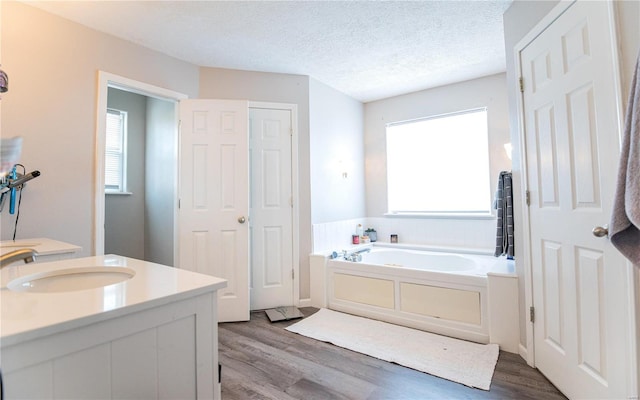 bathroom with a textured ceiling, wood-type flooring, vanity, and a bathing tub