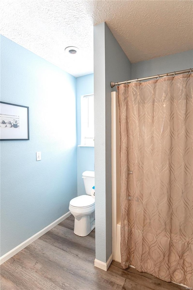 bathroom with a textured ceiling, hardwood / wood-style floors, toilet, and shower / bathtub combination with curtain