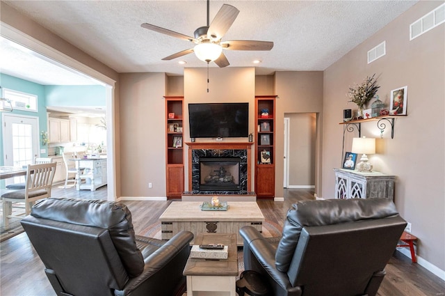 living room with a premium fireplace, ceiling fan, a textured ceiling, and dark hardwood / wood-style flooring