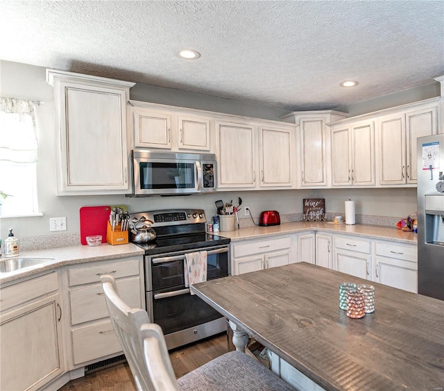 kitchen with appliances with stainless steel finishes, dark hardwood / wood-style floors, sink, and a textured ceiling