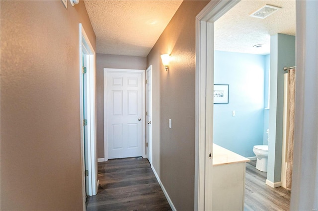 corridor with a textured ceiling and wood-type flooring