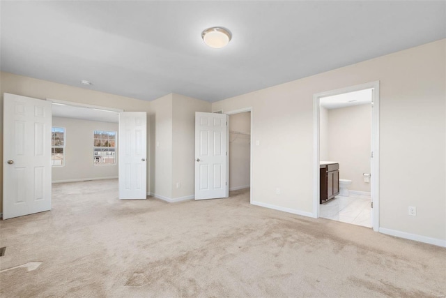 unfurnished bedroom featuring light carpet, ensuite bath, a closet, and a spacious closet