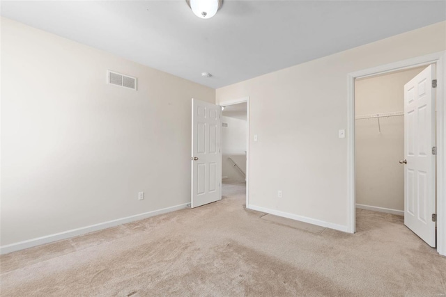 unfurnished bedroom featuring a walk in closet, light colored carpet, and a closet