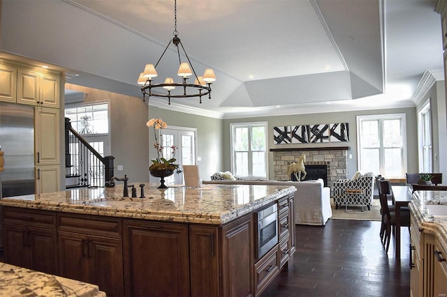 kitchen featuring a stone fireplace, crown molding, built in appliances, decorative light fixtures, and a tray ceiling