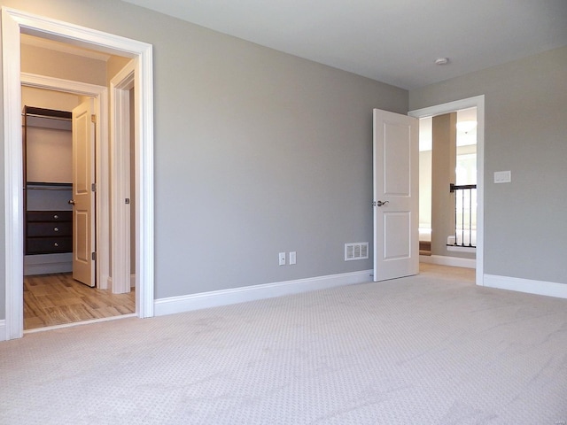 unfurnished bedroom featuring a spacious closet, light carpet, and a closet