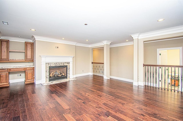 unfurnished living room featuring dark wood-type flooring, a fireplace, built in desk, ornamental molding, and ornate columns