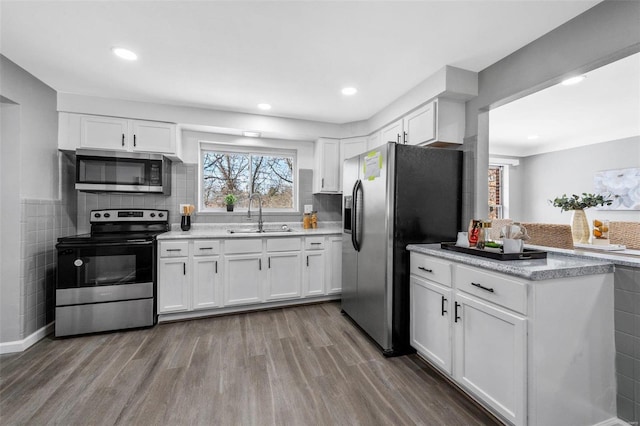 kitchen with sink, white cabinetry, stainless steel appliances, decorative backsplash, and light wood-type flooring