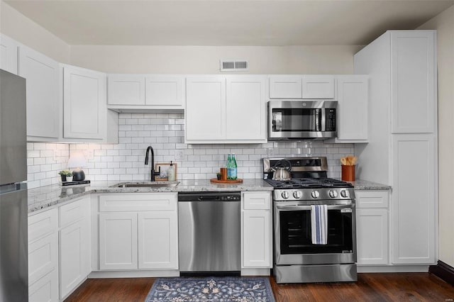 kitchen featuring stainless steel appliances, sink, white cabinetry, backsplash, and light stone countertops