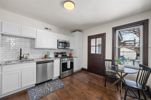 kitchen featuring stainless steel appliances, sink, white cabinetry, light stone counters, and tasteful backsplash