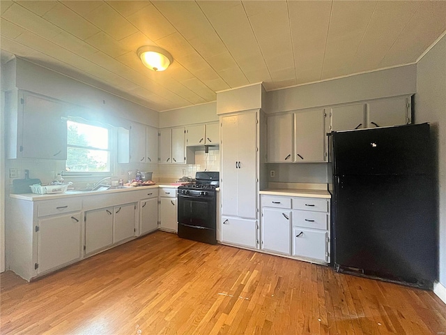 kitchen featuring sink, white cabinetry, light wood-type flooring, backsplash, and black appliances