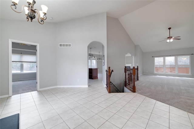 carpeted spare room featuring ceiling fan with notable chandelier, a healthy amount of sunlight, and high vaulted ceiling