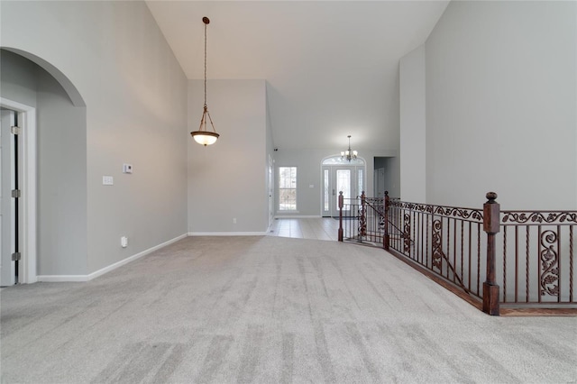 carpeted empty room featuring an inviting chandelier and high vaulted ceiling