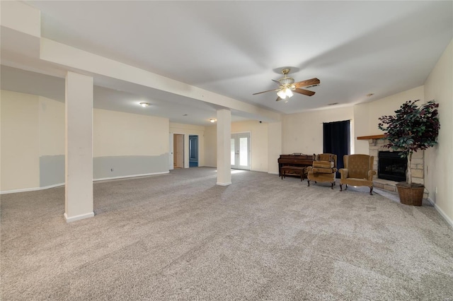 sitting room with a stone fireplace, carpet floors, and ceiling fan