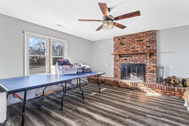 game room with a brick fireplace, dark hardwood / wood-style flooring, and ceiling fan