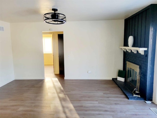 unfurnished living room featuring hardwood / wood-style flooring, an inviting chandelier, and a brick fireplace