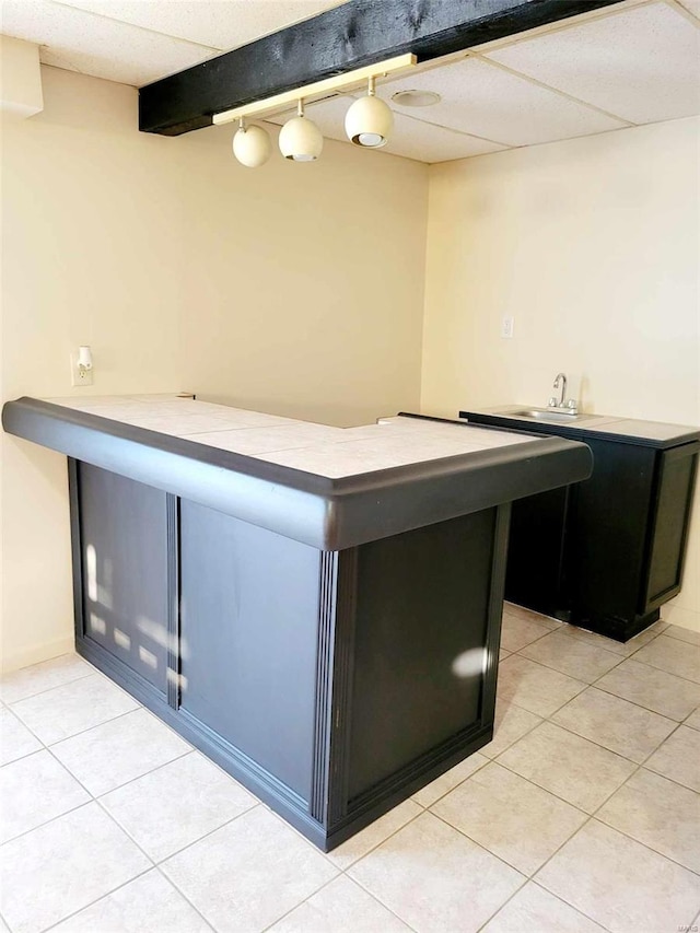 bar featuring a paneled ceiling, decorative light fixtures, sink, and light tile patterned floors