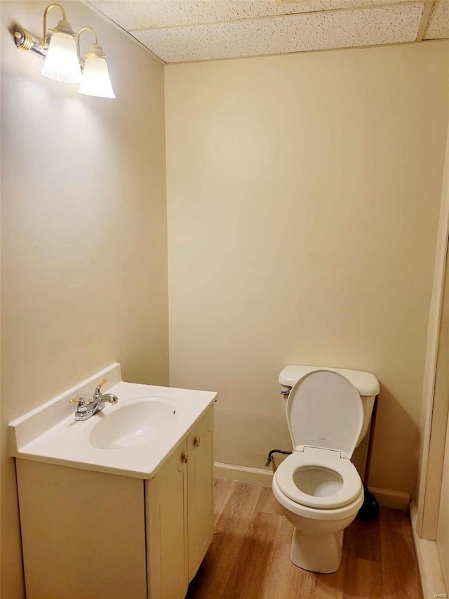 bathroom with a paneled ceiling, wood-type flooring, toilet, and vanity