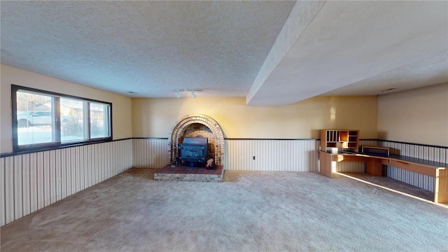 unfurnished living room featuring carpet flooring, a wood stove, and a textured ceiling