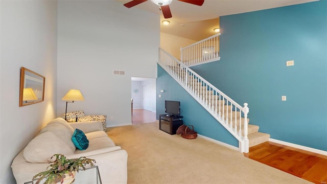 carpeted living room featuring ceiling fan and a towering ceiling