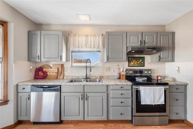 kitchen with backsplash, sink, light wood-type flooring, appliances with stainless steel finishes, and gray cabinetry