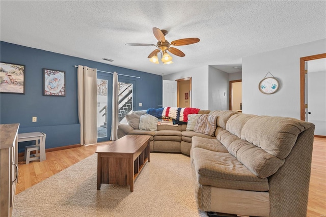 living room with a textured ceiling, ceiling fan, and light wood-type flooring