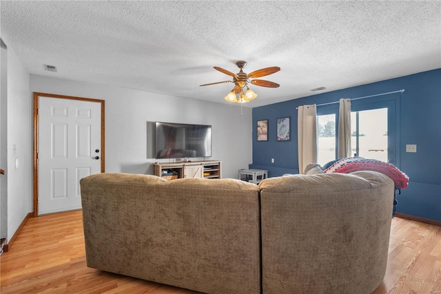 living room featuring ceiling fan, a textured ceiling, and light wood-type flooring