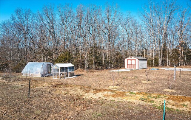 view of yard featuring a storage shed, a view of trees, an exterior structure, and an outdoor structure