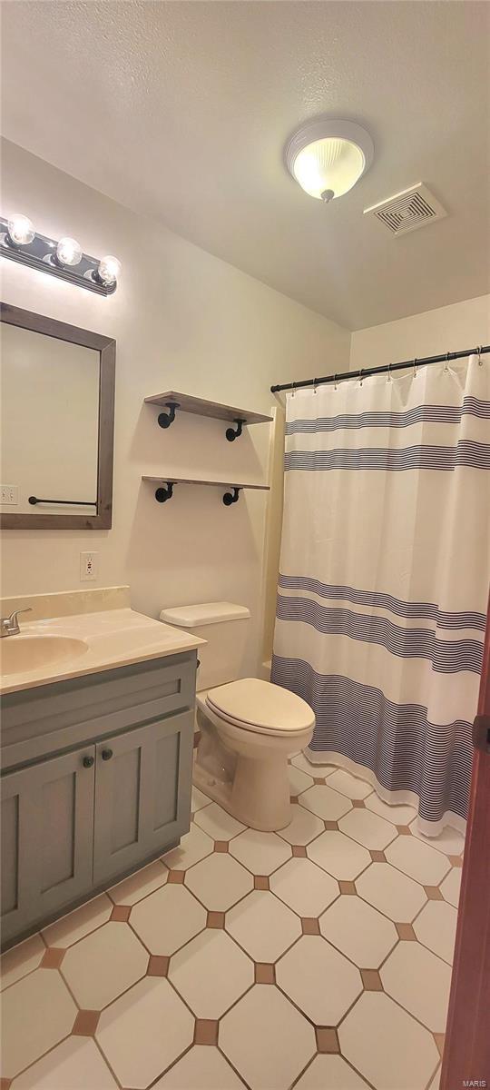 full bathroom featuring curtained shower, visible vents, toilet, vanity, and tile patterned floors