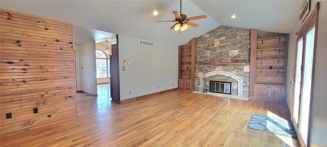 unfurnished living room with ceiling fan, high vaulted ceiling, a stone fireplace, visible vents, and light wood-style floors