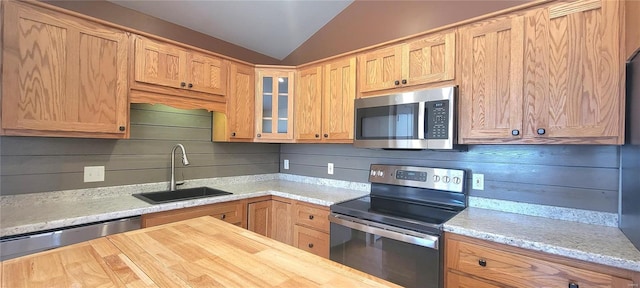 kitchen with lofted ceiling, butcher block countertops, glass insert cabinets, stainless steel appliances, and a sink