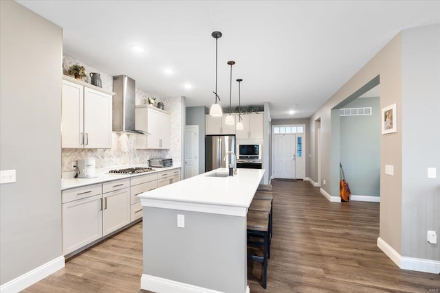 kitchen featuring visible vents, a breakfast bar, wood finished floors, appliances with stainless steel finishes, and wall chimney exhaust hood