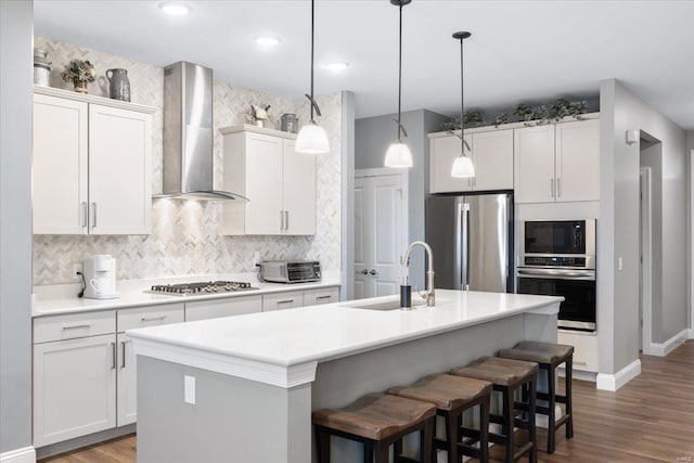 kitchen with backsplash, wall chimney range hood, an island with sink, stainless steel appliances, and a sink