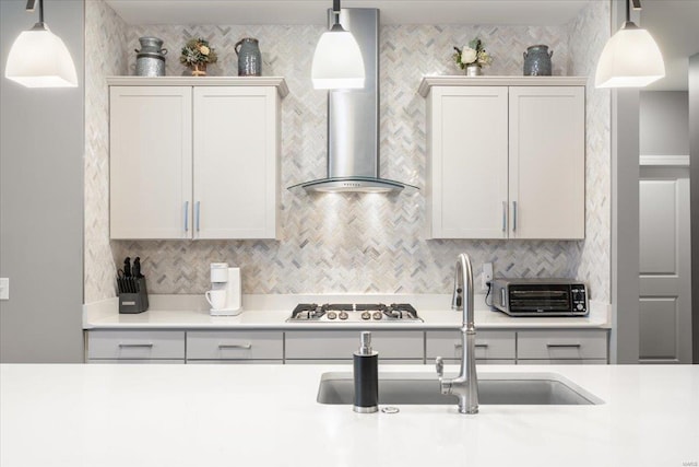 kitchen with a sink, wall chimney range hood, light countertops, and stainless steel gas cooktop